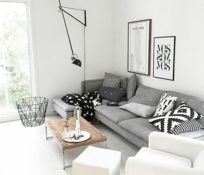 akcento spalvos pilkai, pilkai kampinei sofai, baltam foteliui ir osmanui, mediniam kavos staliukui, įrėmintam pakabinamam menui