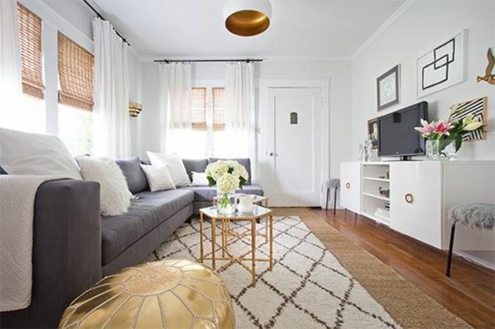 pilka aksominė sofa, spalvos, derančios prie pilkų sienų, auksinis pufas, mažas stiklas ir žalvaris, kavos staliukas