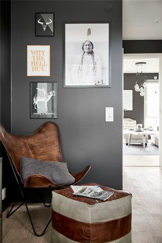 kokios spalvos antracito pilkos spalvos koridorius, rudos odos fotelis ir rudos bei pilkos odos išmatos, pilka siena su paveikslėliais juoduose rėmuose, grindys padengtos lygiu PVC parketu