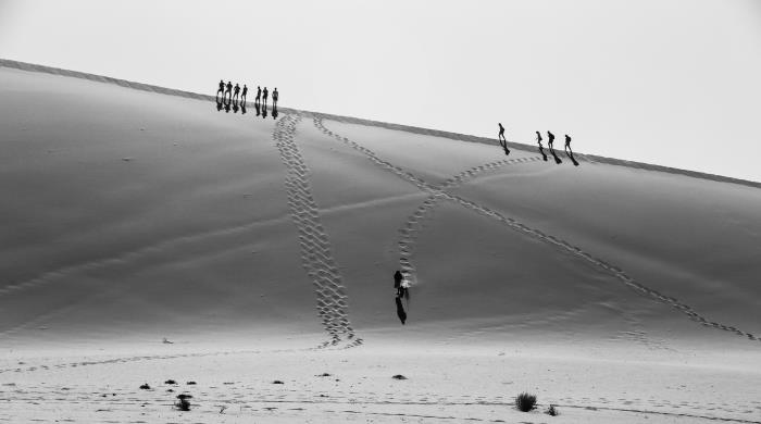 črno -bele puščavske pokrajinske silhuete moških, ki hodijo po peščeni sipini in za seboj puščajo sledi
