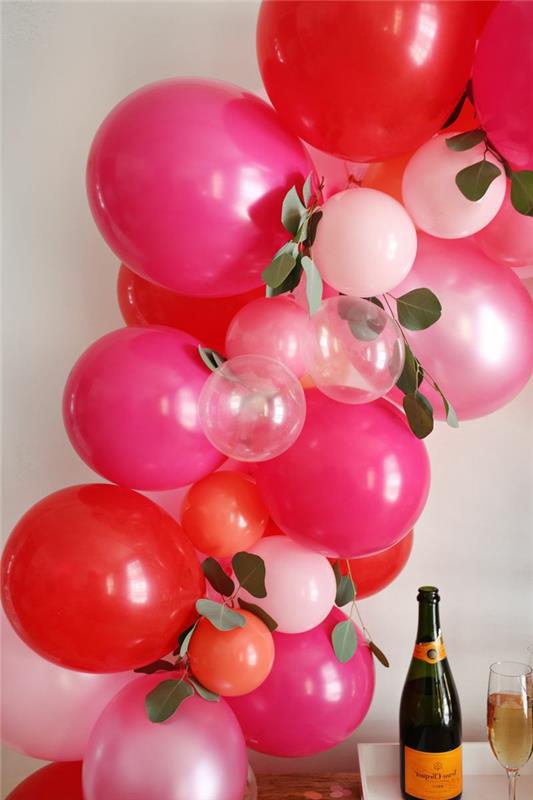 dideli ciklamenų balionai ir maži rožiniai ir skaidrūs balionai, dekoratyviniai lapai, butelis šampano ir taurė