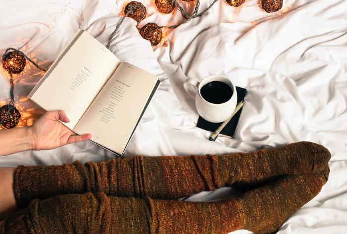 modernus jaukus miegamojo dekoras, šviesi girlianda, ilgos kojinės, kava ir knyga