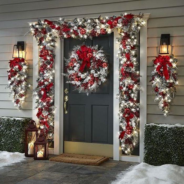 Kırmızı ve gümüş topları olan Noel dış mekan ışık çelengi, kapının önünde kurdelelerle birleştirilmiş iki fener.