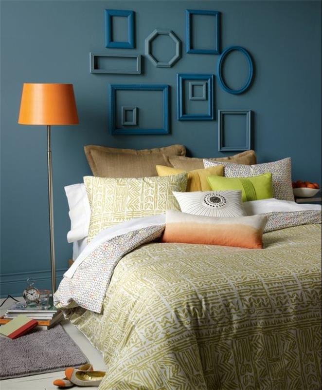 dekor za spalnico, modro stene, posteljne prevleke in blazine v beli, zeleni, bež, rjavi in ​​rumeni barvi, prazen dekor okvirja, več ovalnih, pravokotnih in kvadratnih okvirjev, oranžna svetilka
