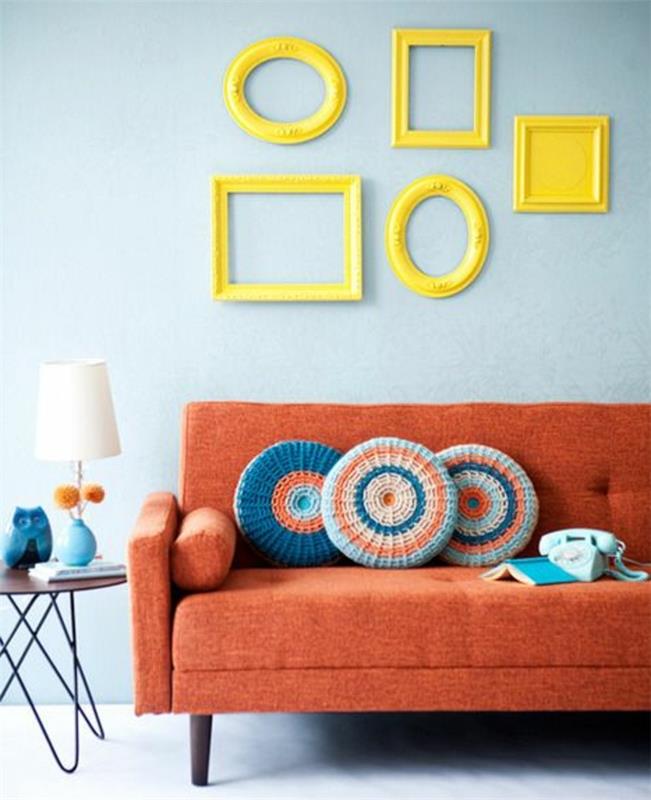 deco prazen okvir z rumenimi ovalnimi in pravokotnimi okvirji, asimetrična razporeditev, oranžna zofa, stranska miza iz lesa in kovine, oblikovalska svetilka