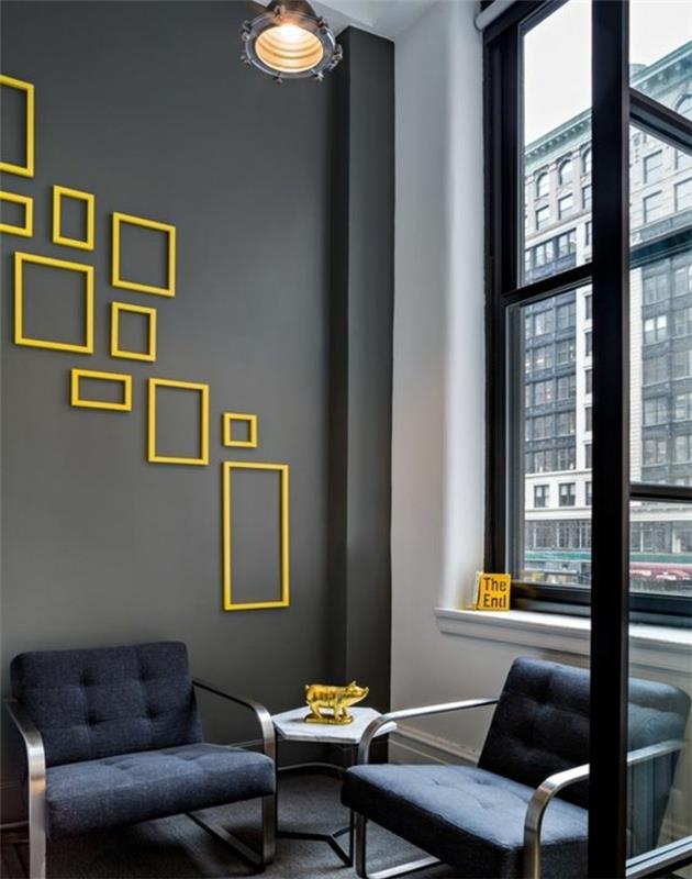stena iz praznih rumenih okvirjev, različnega formata, antracitno siva barva stene, temno modri naslanjač, ​​okras z zlatim prašičem, industrijska viseča svetilka