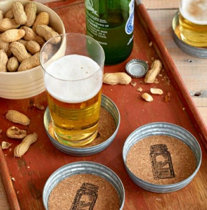 ročno izdelani podstavki za medveda, na rjavem pladnju, s kozarcem in steklenico piva ter jedjo arašidov, na leseni mizi