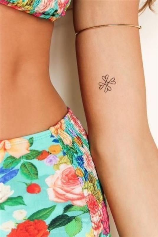 moteris dėvi gėlėtą maudymosi kostiumėlį, mažos gėlės širdies dilbio tatuiruotę, mažas tatuiruotes, auksinę apyrankę