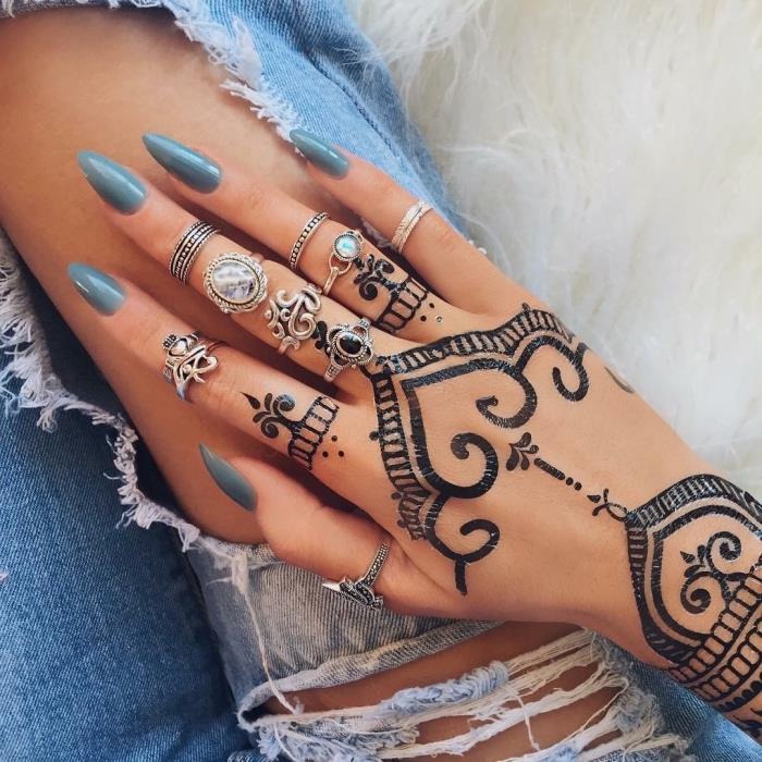 model ročne kane, manikura z dolgimi nohti in temno modrim lakom, kovinski nakit in etnična tetovaža