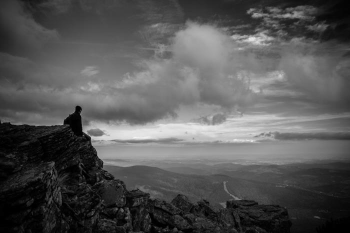 lepa fotografija moškega, ki sedi na skali in razmišlja o naravi pod očmi oblakov, črno -beli portret človeka in gore