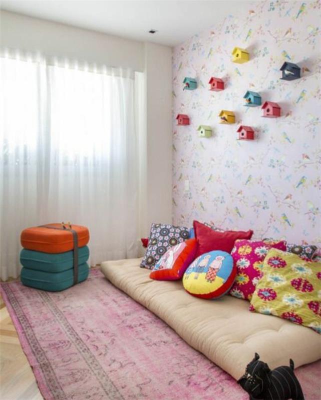 idėja, kaip sutvarkyti vaiko kambarį pagal Montessori pedagogiką, dėvėtas raudonas kilimas, čiužinys ant grindų, įvairiaspalvės pagalvėlės, tapetai, gėlių raštai, paukščių lesyklėlės siena