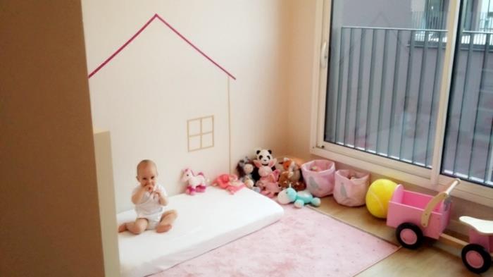 montessori apstatymo metodas, baltas čiužinys, rožinis kilimas, žaislai, žaislų dėžutės, dramblio kaulo siena, namo sienų dizainas