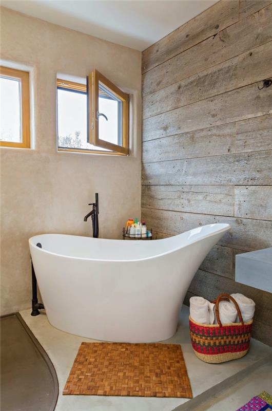 laisvai stovintis klubo vonios modelis mažame vonios kambaryje su medžio efekto sienomis ir grindimis baltos ir pilkos spalvos