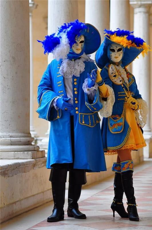 mėlyna pora, dėvi venecijietiškas kaukes, dideles karnavalines kepures, ilgus juodus batus, baltus stulpus