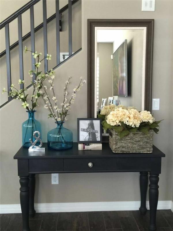 stačiakampis veidrodis, turkio spalvos vazos su žydinčiais stiebais, juodas stalas, kaimiškas krepšelis