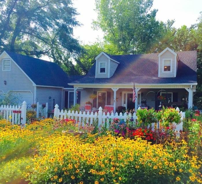 na primer, angleški vrtni model, rumeno cvetje in druge barve, gredica, urejena v bližini bele ograje, kmečka hiša