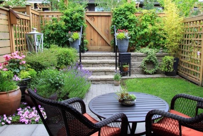 mažas sodo išdėstymo modelis, sodo baldai, austas stalas ir kėdės, maža veja, gėlių lova ir krūmai, tvora ir medinė pertvara