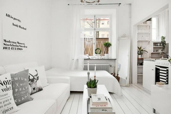 Küçük beyaz bir stüdyoda İskandinav mobilyaları, beyaz yatak ve kanepe, hafif parke, beyaz sehpa, beyaz mutfak cephesi, yeşil bitkiler, siyah beyaz alıntı posteri