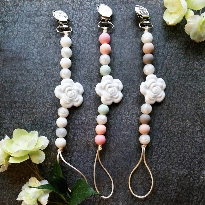 rafinuotas ir minkštas individualizuotas čiulptuko modelis, pagamintas iš pastelinių spalvų perlų, papuoštas gražia balta gėle grandinės viduryje