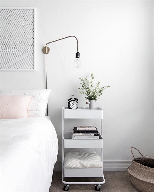 Beyaz renkte İskandinav yatak odası dekorasyon fikri, pembe minder ve raflı tekerlekler üzerinde beyaz komodin, gri halı