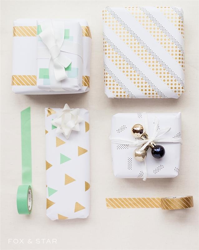 Kalėdinė dovanų dėžutė, įvyniota į baltą popierių su puošmena trikampiais ir „washi“ juostos juostelėmis, juostele ir mažais kalėdiniais kamuoliukais