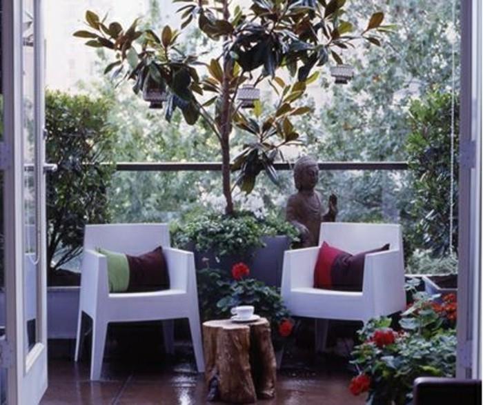ureditev ozkega balkona, beli stoli, okrašeni s pisanimi blazinami in majhno klubsko mizico iz debla, kipcem Bude, zelenimi rastlinami in zen cvetočimi rastlinami