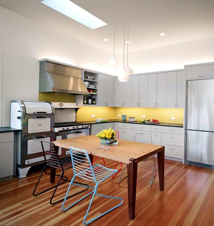 sarı bir sıçrama ve bistro tarzı yemek alanı ile canlandırılan renkli ve endüstriyel vurgulara sahip modern bir gri mutfak