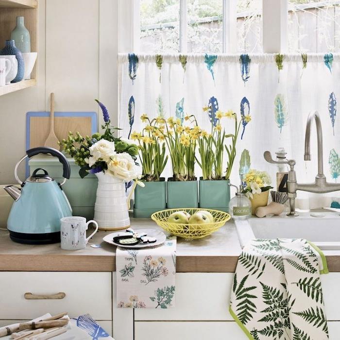 dodatki celadon blue deco, bela kuhinjska omara z leseno delovno ploščo in lesenimi policami, več zelenih rastlin, zavesa z modrim, zelenim in vijoličnim perjem