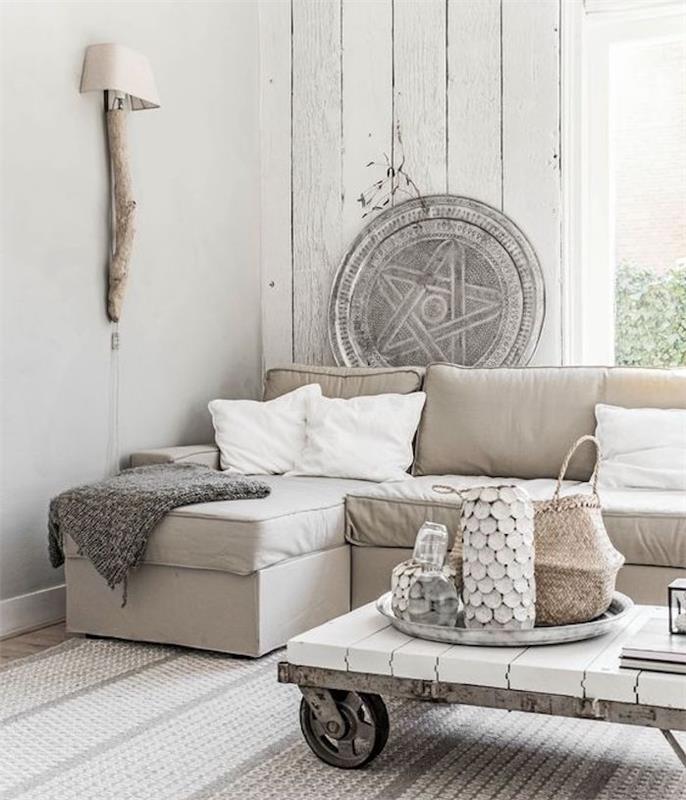 sivo -bela postavitev dnevne sobe, biserno siv kavč, svetlo senčnik, bele blazine in mizica s kolesi, naravni dekor, leseni poudarki