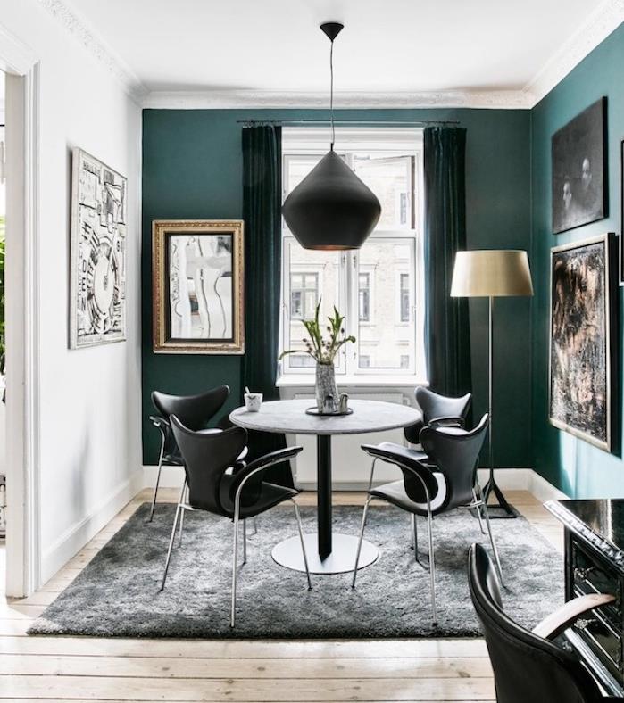 račja modra deko dekoracija, naftni odtenek na enem delu stene, parket iz svetlega lesa, siva miza, obdana s črnimi stoli, ogljeno siva preproga, črna suspenzija, stenska dekoracija abstraktnih okvirjev za slikanje