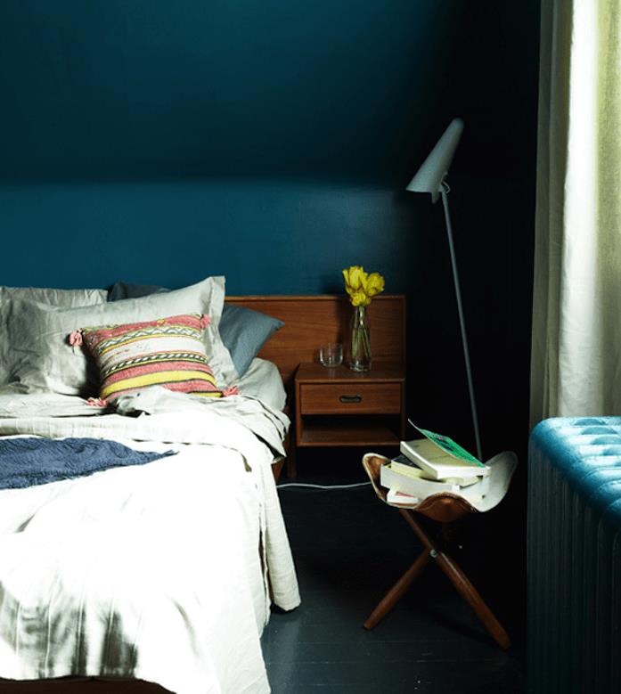 petrolej modra barva za spalnico pod pobočjem, sivo posteljnino, leseno nočno omarico, antracit siv parket, stol za shranjevanje knjig