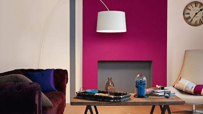 bordo spalvos sofa ir aviečių spalvos židinio siena, kaimiškas medinis stalas, baltas pasukamas fotelis