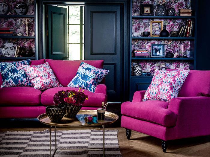 aviečių spalvos sofa ir fotelio idėja tamsiai tamsiai mėlynos spalvos gyvenamajame kambaryje, zebrinis kilimas, auksinis rytietiškas kavos staliukas, mėlyna knygų spinta, neįprasti dekoratyviniai aksesuarai