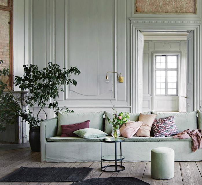celadon zelena dnevna soba v beli barvi sten in sivo zelena zofa, rjavi parket, zelena rastlina, roza, bordo, zelene in pisane blazine, minimalistična črna miza