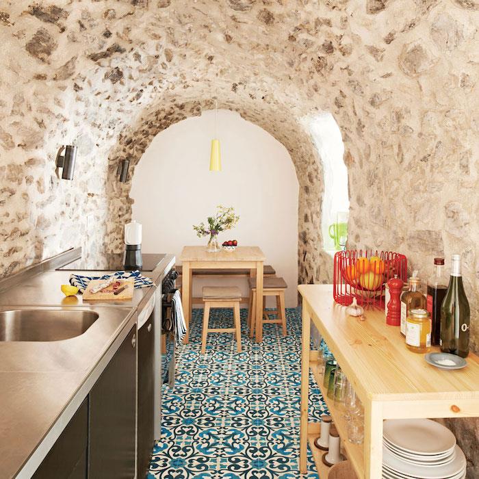 mozaik yer karoları, paslanmaz çelik aletler ve ahşap ada masası ile orijinal bir Fas dekorlu mutfakta taş duvarlar