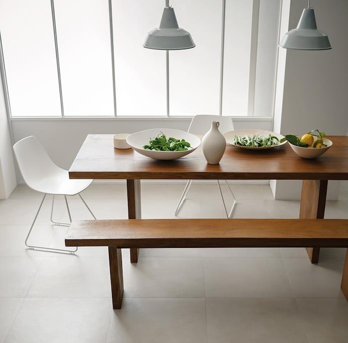 jedilnica s keramičnimi tlemi v barvi greg, miza in klop iz masivnega lesa, beli skandinavski stoli, svetlo sive viseče luči, bele stene