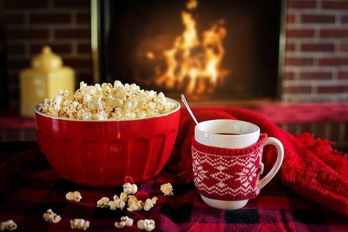 puodelis karšto šokolado, dubuo, pripildytas spragintų kukurūzų, raudonos antklodės, romantiškas židinys, gurmaniška atmosfera, kalėdinis fonas