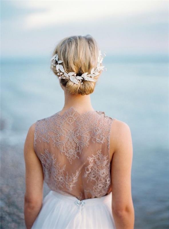 lahka ideja o pričeski s punđo, dolgi blond lasje, krona belega umetnega cvetja, elegantna poročna obleka