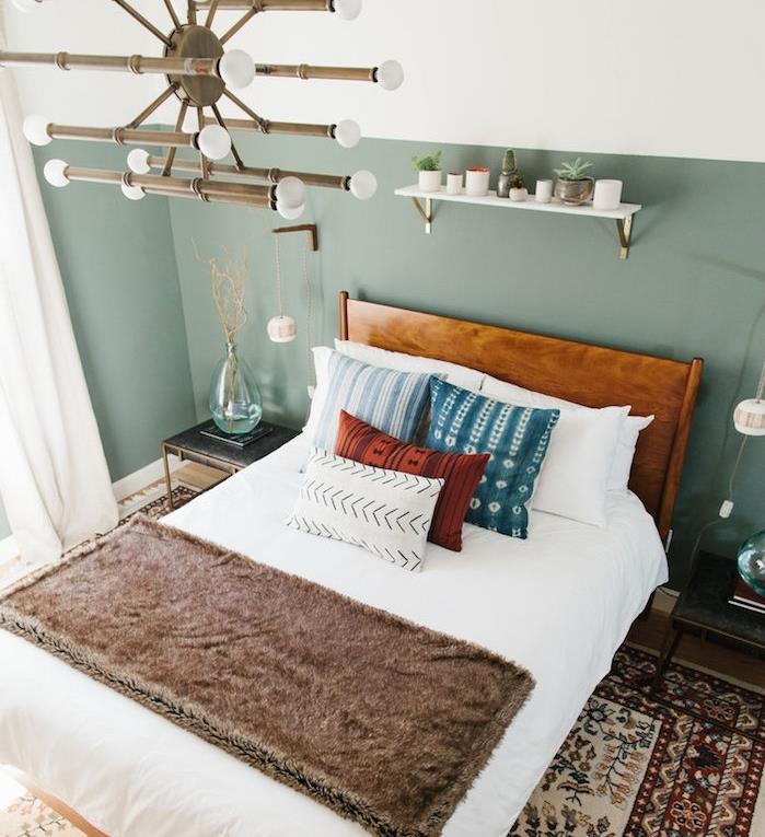 oblikovalska spalnica z barvnimi stenami, kot vzglavje, originalni lestenec, lesena postelja z belim posteljnino, modre, rdeče in bele blazine, orientalska preproga, bela polica za shranjevanje majhnih rastlin