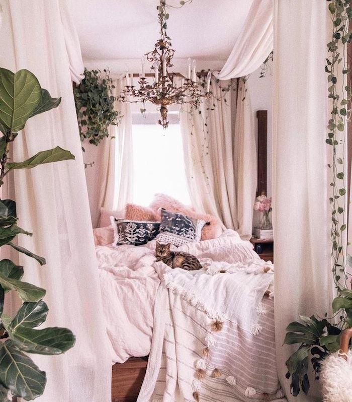 prašmatnus bohemiškas miegamasis su lova su baldakimu, patalynės sluoksnis, dekoratyvinės kokoninės pagalvėlės, originali miegamojo liustra, žalių augalų interjero apdaila