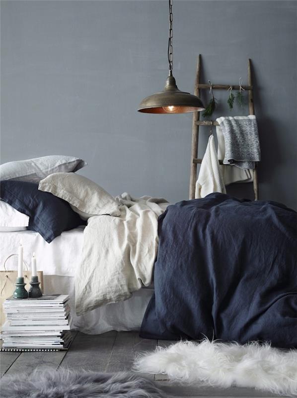dekoriranje spalnice, siva stena, belo in mornarsko modro posteljnino, siv parket, okrasne lesene lestve, industrijska viseča svetilka