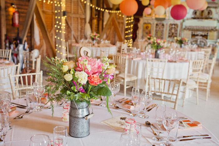 kaimo vestuvės, balta staltiesė, pieno ąsotis, užpildytas kaimo gėlėmis, spalvingi žibintai ir lengva girlianda