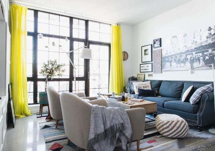 gri koltuklar, koyu mavi kanepe, geometrik desenli gri halı, sarı perdeler, siyah beyaz fotoğraf duvar dekorasyonu ile modern oturma odası düzeni