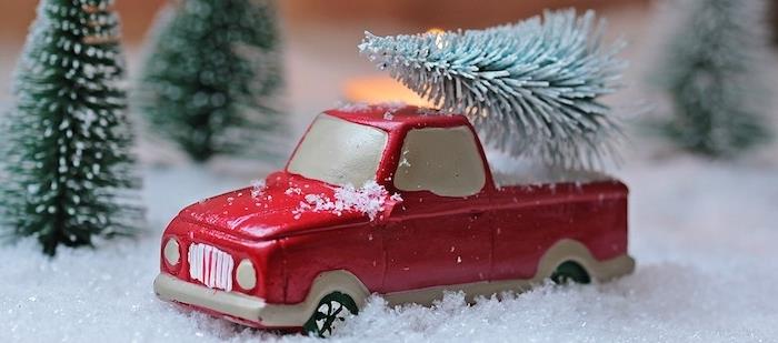 Kalėdų tapetai raudoname miniatiūriniame automobilyje ant dirbtinio sniego ir žalių medžių