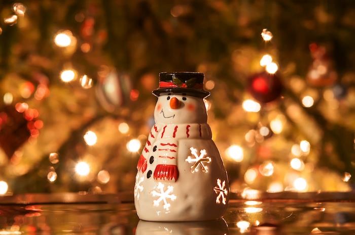 Kalėdų tapetai sniego senelio figūrėlės žvakidėje su papuošta eglute fone