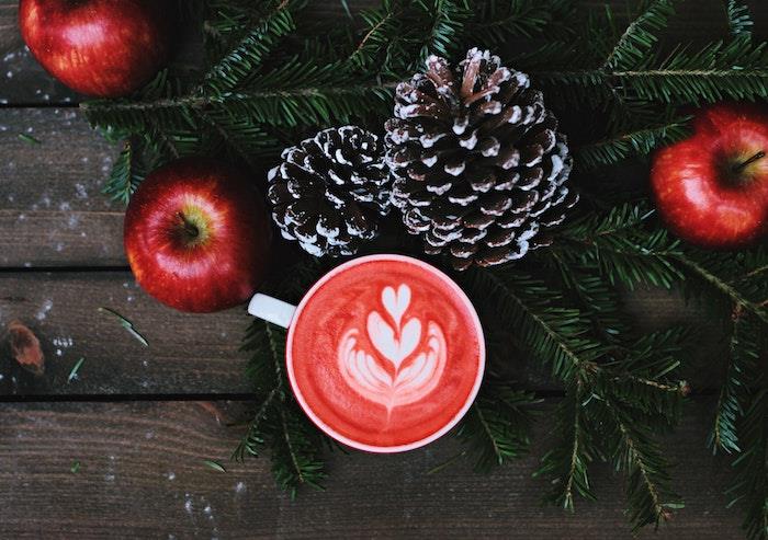 Kalėdų fono idėja, karštas gėrimas, sidro raudoni obuoliai, kankorėžiai ir žalios pušies šakos ant medinio stalo