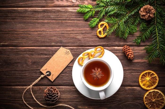 Kalėdinių tapetų idėja karštoje arbatoje baltame puodelyje, kankorėžiai, citrinos skiltelės, žalios pušies šakos