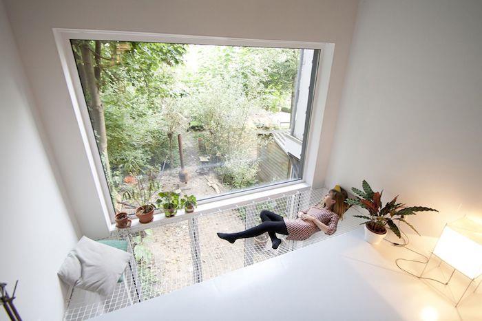 minimalistična deko v beli barvi z izvirno notranjo visečo mrežo s pogledom na zunanjo stran skozi veliko okno, zelene rastline naokoli