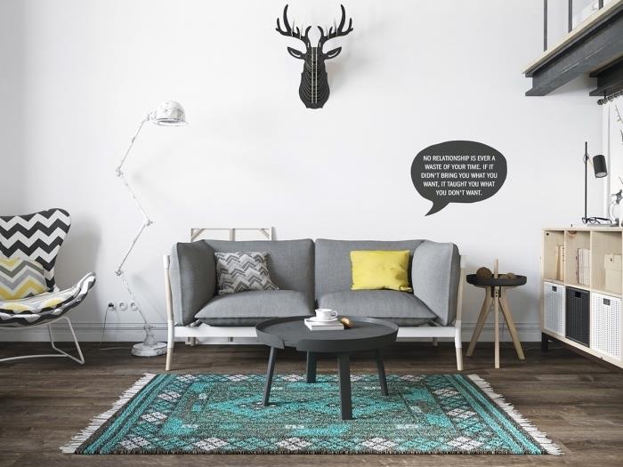 İskandinav mobilyaları, gri kanepe ve sehpa, gri ve mavi halı, kahverengi parke, beyaz, gri ve sarı koltuk, av kupası duvar dekorasyonu