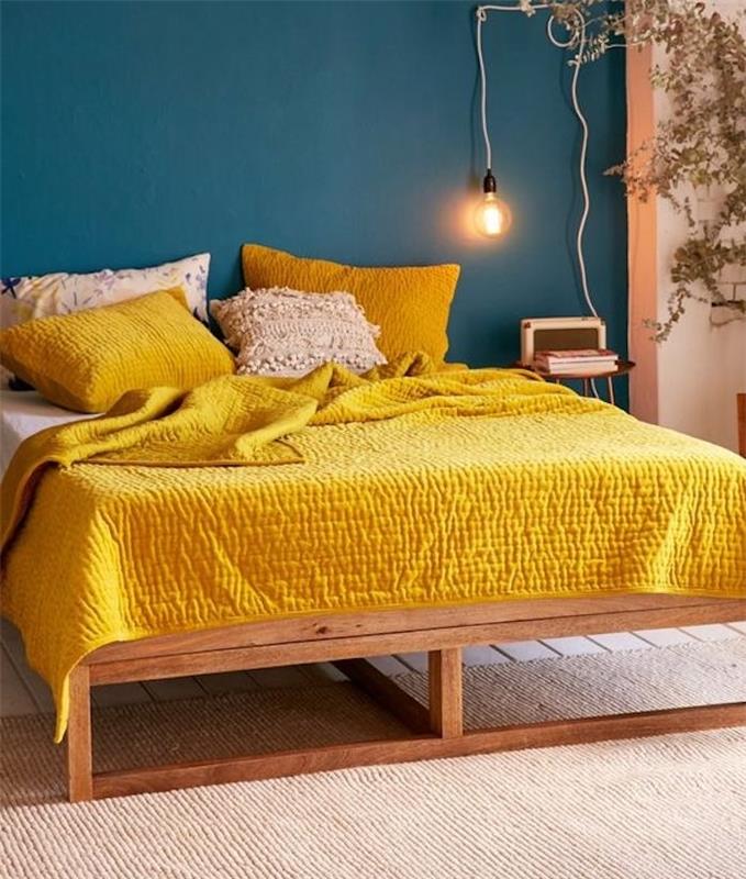 del stenskega odtenka modre, barve nafte, lesena postelja, belo in rumeno posteljnino, nočna svetilka z električno žarnico, bež preproga, zelena rastlina